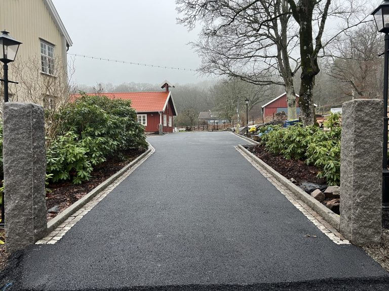 Asfalterad villauppfart med murade grindstolpar