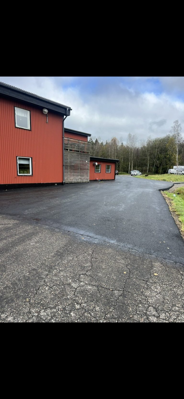 Asfalterad uppfart framför rött bostadshus